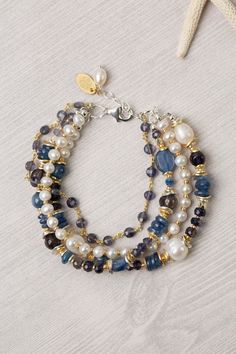 three strand bracelet with blue and white beads on a starfish hook chain, next to a seashell