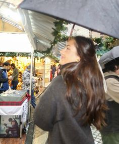 a woman holding an umbrella in front of a store filled with people and christmas decorations