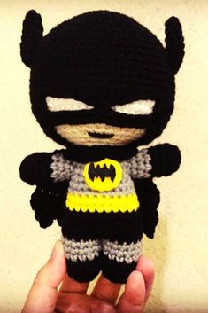 a crocheted batman doll is being held by someone's hand in front of a wall