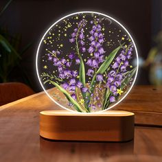 a glass vase with purple flowers in it sitting on a wooden table next to a potted plant