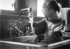 a little boy that is standing in a sink with water coming out of the faucet