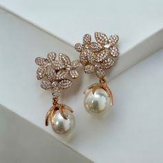 Make a stunning statement this season with the gorgeous Flowers Pearl Earrings. These elegant earrings feature an exquisite floral-inspired design for timeless sophistication. Three delicate blossoms set as if in a bouquet boast an abundance of dazzling cubic zirconia on each petal with a beautiful pearl dangling provocatively beneath, giving it an extra special touch of sophistication. Pearls are an elegant, classic choice that will never go out of style. This timeless gemstone will take you to every significant event of your life. Whether you're the stylish bride with a taste for timeless elegance, or just wanting to add a dash of sparkle to your everyday wardrobe, these earrings will be all you need. Handcrafted in 925 sterling silver dipped in 18ct rosegold. Pearls. Cubic zirconia.  Pa Elegant Rose Gold Pearl Earrings For Evening, Elegant Rose Gold Bridal Earrings With Elegant Design, Rose Gold Elegant Bridal Earrings, Formal Rose Gold Pearl Earrings With Elegant Design, Luxury Rose Gold Pearl Drop Earrings, Luxury Rose Gold Drop Pearl Earrings, Elegant Rose Gold Bridal Earrings For Evening, Elegant Rose Gold Jewelry For Mother Of The Bride, Formal Rose Gold Earrings With Rose Design