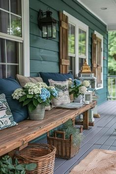 a wooden bench sitting on top of a porch next to a blue house with flowers