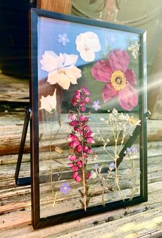 a glass frame with flowers in it on a wooden table next to a potted plant