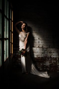 a woman in a wedding dress leaning against a brick wall with her hands on her head