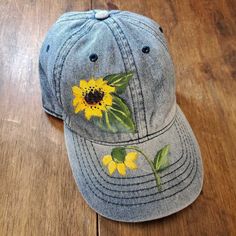 a denim cap with yellow flowers painted on it sitting on a wooden floor next to a pair of scissors