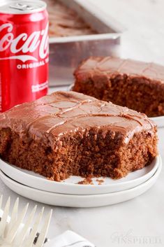 a piece of chocolate cake on a plate with a cup of coke in the background