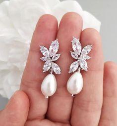 a pair of white pearl and crystal earrings in the palm of someone's hand