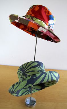 two hats are placed on top of each other in a display stand with a white wall behind them