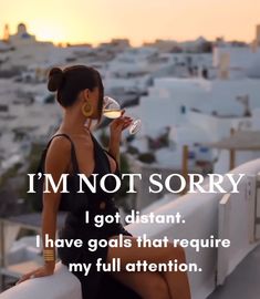 a woman sitting on top of a roof drinking from a wine glass with the sun setting in the background