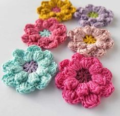 four crocheted flowers sitting on top of a white table next to each other