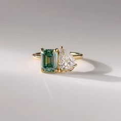 an emerald and diamond ring with two pear shaped diamonds on the side, set in yellow gold