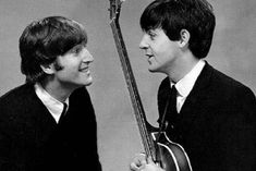 two young men are holding guitars and smiling at each other while the man is wearing a suit