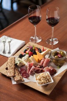 a wooden table topped with two wine glasses filled with red wine and assorted food