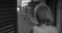 a woman standing in front of a window looking out at an alleyway with buildings