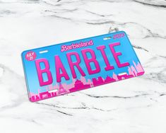 a pink and blue license plate with the word barbie on it sitting on a marble surface