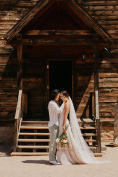 a bride and groom standing in front of a wooden building with steps leading up to it