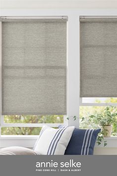 a living room with two windows covered in roman blind shades and pillows on the couch