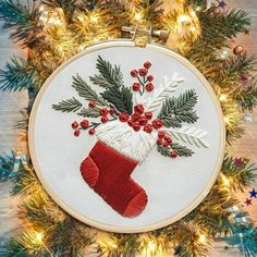 an embroidered christmas stocking with holly and red berries on it is hanging from a tree