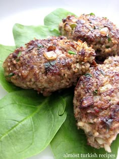 three meat patties with spinach leaves on a white plate