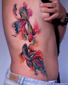 a woman's stomach with watercolor tattoos on her body and an image of two fish