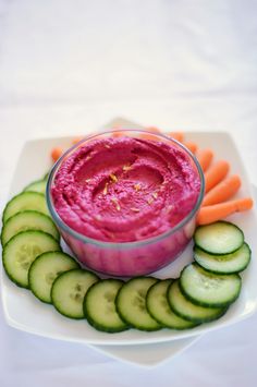 a white plate topped with cucumber and carrots next to a bowl of dip