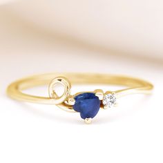 a yellow gold ring with a blue sapphire and two white diamonds on the side, sitting on a plain surface