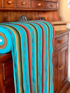 a blue and green striped blanket sitting on top of a wooden dresser next to drawers