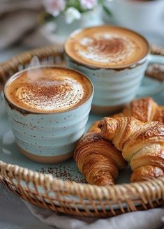 two croissants sitting on top of a blue plate next to some coffee cups