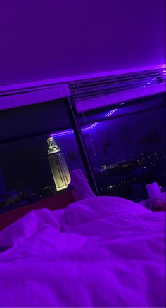 a bed with white sheets and purple lights on the wall next to a large window