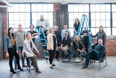 a group of people standing and sitting around each other in front of windows with ladders