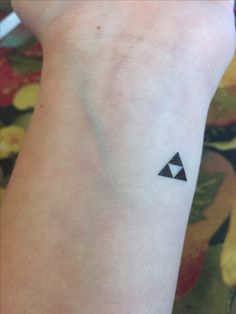 a small black triangle tattoo on the left inner arm, with an arrow in the middle