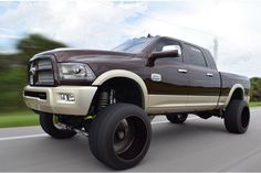 a brown and white truck driving down the road with big tires on it's sides