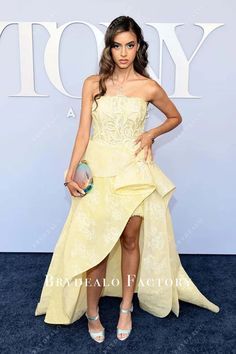 a woman in a yellow dress standing on a blue carpet with her hand on her hip