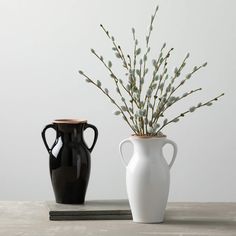 two black and white vases sitting next to each other on a table with flowers in them