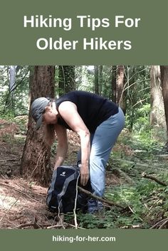 a man bending over in the woods with his backpack