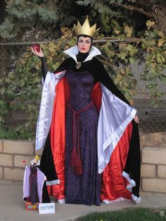 a woman dressed up as evil queen standing in front of a fence with her hand out