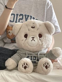 a woman sitting on top of a bed holding a teddy bear in her hand and wearing a gray shirt