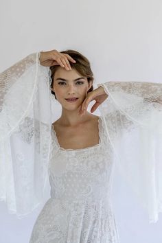 a woman is posing with her arms behind her head, wearing a white dress and long sleeves