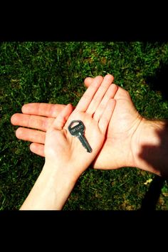 two hands holding a small key tattoo on their palms, with grass in the background