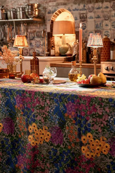 the table is covered with colorful flowers and fruit, along with two lamps on either side