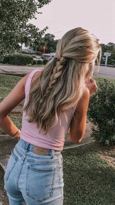 a woman with long hair wearing jeans and a pink tank top is standing in the grass