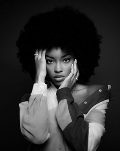 a black and white photo of a woman holding her hands to her face with an afro hairstyle