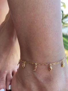 COLOR: GOLD PLATED MATERIAL: STAINLESS STEEL The "Under The Sea" gold-plated jewelry anklet from Dainty By Gio! This gorgeous piece is inspired by the beauty of the ocean and beach, and features a charming little beach charm that will transport you to the sandy shores with each wear. Crafted with love, including a durable base metal plated with a layer of lustrous gold, this anklet is not only stunning but also affordable. Enjoy the luxury and style of real gold without the hefty price tag! At D Ankle Charm Bracelet, Under The Sea Jewelry, Gold Ocean-inspired Jewelry With Dangling Charms, Ocean-inspired Gold Jewelry With Dangling Charms, Beachy Gold Jewelry With Starfish Charm, Gold Strand Anklets For Vacation, Gold Starfish Charm Jewelry For Beach, Gold Beach Jewelry With Starfish Charm, Gold Jewelry With Starfish Charm For Beach