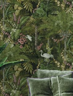 a green couch sitting in front of a wall covered with plants and birds on it