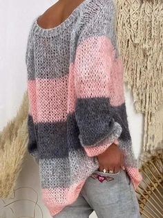 a woman standing in front of a wall wearing a pink and grey sweater with stripes on it