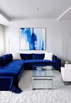 Design a contemporary living room that blends bold blue tones with crisp white accents for a striking yet elegant aesthetic. Feature a modern sectional sofa in a rich royal blue, set against white walls with large abstract art pieces. Include a high-end glass coffee table with minimalistic chrome legs, and a few white accent chairs with sleek lines. A luxurious blue velvet throw and decorative pillows should add texture and warmth. Install recessed lighting in the ceiling and a \ Contemporary Chic Living Room, Installing Recessed Lighting, White Accent Chair, Modern Sofa Sectional, Elegant Aesthetic