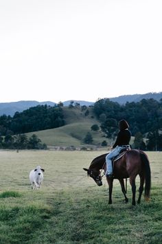 a woman riding on the back of a brown horse next to a white dog in a field