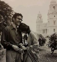 a man and woman standing next to each other in front of a large white building