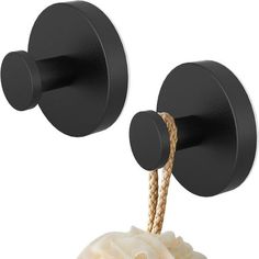 two black wall mounted hooks with rope attached to the back of each hook, one holding a soap bar